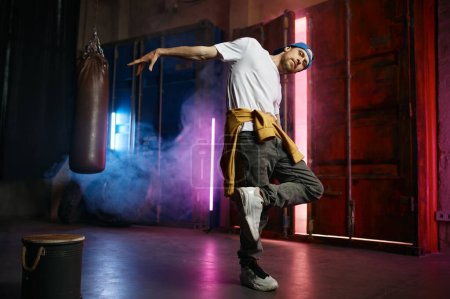 Foto de Cool y feliz bailarina callejera de hip hop en ropa de moda bailando sobre fondo de estudio loft. Concepto Breakdance - Imagen libre de derechos