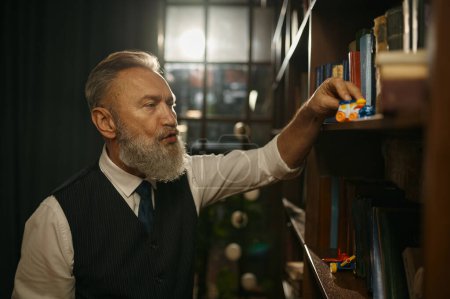 Foto de Hombre de negocios sénior con atuendo anticuado jugando al tren de juguete en la estantería de la biblioteca de casa u oficina - Imagen libre de derechos