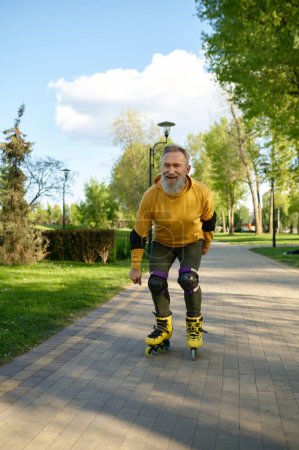 Photo for Happy playful mature man rollerskating on pathway in city park. Senior male feeling joy and fun during active sports recreational time on weekend - Royalty Free Image