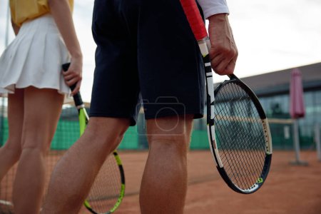 Téléchargez les photos : Vue rapprochée sur raquette de tennis en main du joueur masculin et féminin sur fond de court extérieur. Mode de vie sain et concept sportif - en image libre de droit