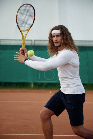 Téléchargez les photos : Sportsman montrant une expression faciale concentrée frappant la balle avec une raquette de tennis jouant sur un terrain ouvert en été - en image libre de droit