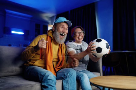 Photo for Expressive senior family couple watching football match on tv at home. Elderly husband and wife feeling overjoyed and excited screaming and cheering favorite soccer game - Royalty Free Image