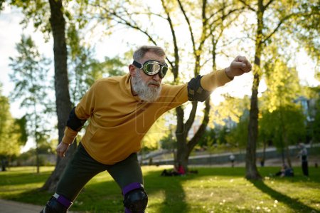 Téléchargez les photos : Homme mature drôle portant des lunettes de conduite rapide sur les patins à roulettes dans la rue de la ville - en image libre de droit