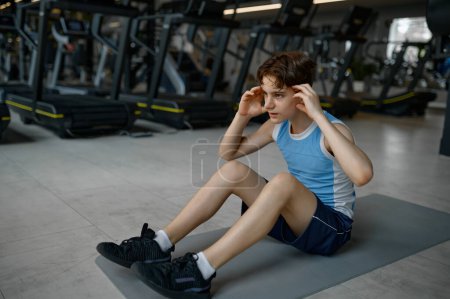 Foto de Fitness adolescente haciendo ejercicio haciendo abdominales para la construcción de músculos abdominales. Entrenamiento en interiores en el gimnasio - Imagen libre de derechos