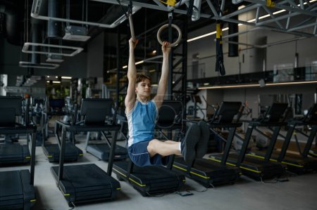 Photo for Strong teenager boy tainting on gymnastics ring at modern gym. Athletic acrobat doing workout exercise on sports equipment indoors - Royalty Free Image