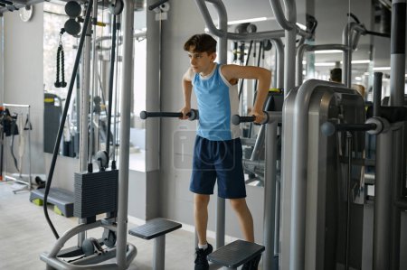 Photo for Muscular teenager boy doing reverse pull-up on sports bar training at gym indoors. Children training and active lifestyle - Royalty Free Image