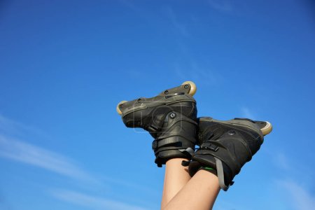 Téléchargez les photos : Pieds humains portant des patins à roulettes dans l'air au-dessus du ciel bleu d'été. Activité sportive et de loisir pendant les vacances d'été - en image libre de droit