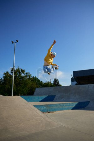 Foto de Adolescente chico disfrutando patinaje sobre ruedas saltar alto. Joven deportista masculino congelado en el aire realizando trucos en skate park. Disparo en movimiento - Imagen libre de derechos