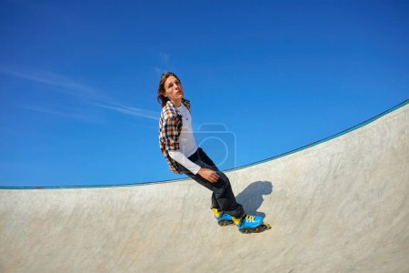 Foto de Adolescente con patines de ruedas que realiza extrema pared-paseo elemento en skate park - Imagen libre de derechos