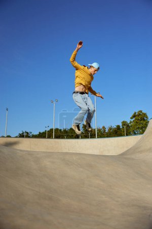 Foto de Adolescente cualificado que usa ropa casual y en patines saltando en la rampa. Patines en línea sport - Imagen libre de derechos