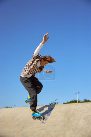 Foto de Niño en patines haciendo acrobacias en rampa de cemento en skate park. Recreación urbana de deportes extremos para adolescentes - Imagen libre de derechos