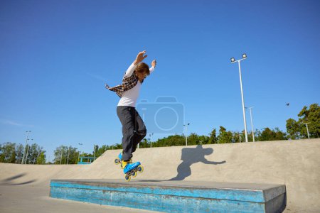 Foto de Joven con patines en línea haciendo acrobacias de equilibrio en el parque de skate. Evento deportivo extremo para adolescentes - Imagen libre de derechos