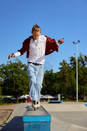 Foto de Patinador adolescente balanceándose en el pedestal realizando trucos de conducción extremadamente. Actividad recreativa en el parque de patinaje en el día de verano - Imagen libre de derechos