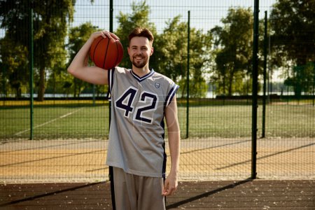 Téléchargez les photos : Portrait en tête d'affiche d'un joueur de basket souriant heureux avec une balle portant l'uniforme - en image libre de droit