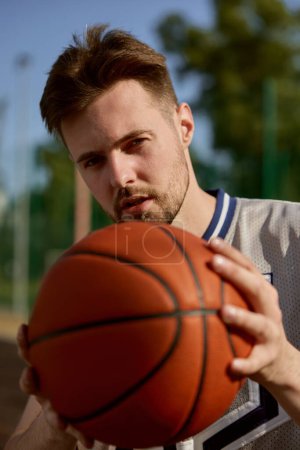 Photo for Closeup face portrait of young basketball player with ball looking in camera. Man athlete exercising outdoors - Royalty Free Image