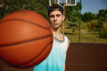 Téléchargez les photos : Gros plan d'un joueur de basket-ball adolescent tenant le ballon devant la caméra. Activité sportive et jeunesse - en image libre de droit