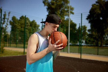 Photo for Teenager basketball player kissing ball praying for score goal and demonstrating good relation for favorite sport game - Royalty Free Image