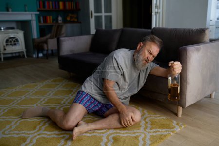 Photo for Senior man addicted to alcohol drinking behind armchair hiding from his wife. Retirement and alcoholism - Royalty Free Image