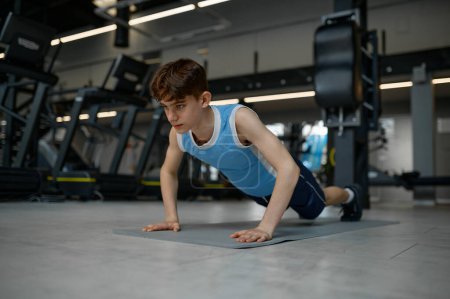 Foto de Adolescente niño sano haciendo gimnasia empuje mientras entrena en el gimnasio. Asistencia sanitaria y autodesarrollo físico - Imagen libre de derechos