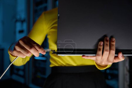 Photo for Closeup on hand of woman connecting internet network cable to laptop in dark server room. Communication technology concept - Royalty Free Image