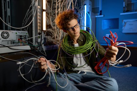 Photo for Confused IT networking engineer looking with disbelief on ethernet cables and optic wires in hands. Difficulty in learning - Royalty Free Image
