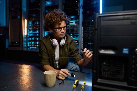 Photo for Young IT technician repairing computer in modern data center. Teenager networking engineer at work - Royalty Free Image