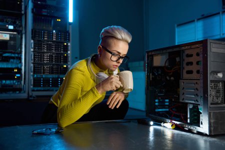 Photo for Young IT technician taking break drinking coffee in dark serve room of modern cloud computing datacenter while working on troubleshooting internet connection failure - Royalty Free Image