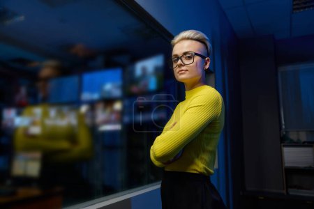 Téléchargez les photos : Portrait d'une jeune travailleuse de centre de données qui regarde une caméra debout dans une salle de serveurs sombre - en image libre de droit