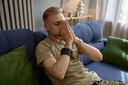 Photo for Depressed soldier suffering from military PTSD sharing his concerns covering face with hands while sitting on sofa at therapy session. Veteran rehabilitation concept - Royalty Free Image