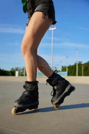 Téléchargez les photos : Gros plan jambes féminines portant des patins à roulettes sur fond de rollerdrom asphalté. Temps de loisirs d'été - en image libre de droit