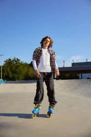 Foto de Joven adolescente en patines haciendo acrobacias en rampa de cemento en skate park. Recreación urbana de deportes extremos para adolescentes - Imagen libre de derechos