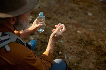 Téléchargez les photos : Homme âgé prenant des pilules médicinales pour éviter le mal des montagnes pendant la randonnée en forêt gros plan - en image libre de droit