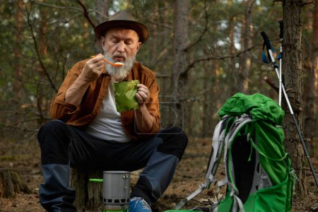Photo for Relaxed senior man hiker eating food taking break after touristic trip in forest. Outdoors adventure on retirement - Royalty Free Image