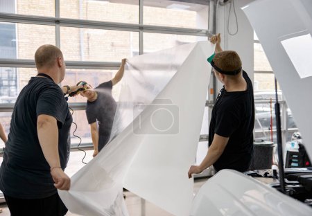 Photo for Car service worker team preparing armored protective ppf film for applying. Cover coating in auto detailing studio garage - Royalty Free Image