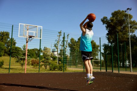 Téléchargez les photos : Adolescent actif jouant au basket sur un terrain extérieur de rue. Jeune garçon sautant avec la balle visant cerceau - en image libre de droit