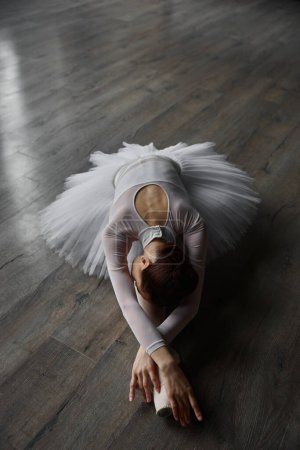 Foto de Joven bailarina elegante esbelta vestida tutú posando en el suelo mientras se entrena en el estudio. Entrenamiento general de ensayo antes de la actuación - Imagen libre de derechos