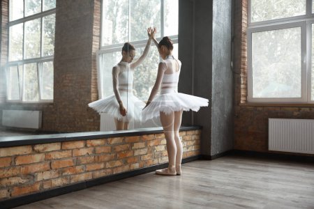 Worried ballerina standing near huge mirror at dance studio feeling nervous before first performance
