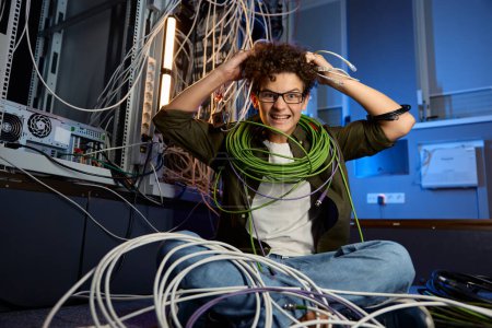 Photo for Stressed teenager geek wrapped in wire sitting on floor in data center. Problem with internet connection cables - Royalty Free Image