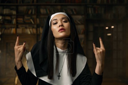 Photo for Portrait of passionate catholic nun gesturing heavy metal rock symbol with two hands. Rock-and-roll music, religion and desire concept - Royalty Free Image