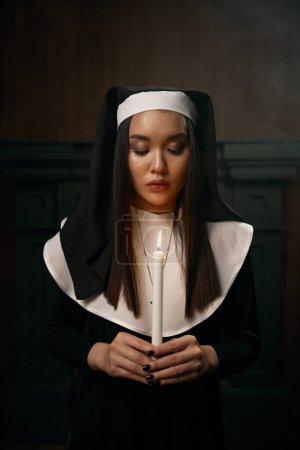 Foto de Retrato de una hermosa monja sosteniendo una vela encendida en las manos mientras rezaba. Voto de obediencia, inocencia y expiación por el concepto de pecados - Imagen libre de derechos