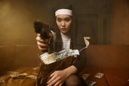 Foto de Mujer segura en bata de monja y tocado apuntando arma de fuego protegiendo sus propios ingresos obtenidos en la venta de cuerpo y servicio íntimo - Imagen libre de derechos