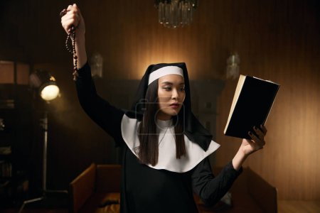 Téléchargez les photos : Jeune religieuse priant avec la bible et des perles avec crucifix dans la chambre nonne simple. Expiation pour les péchés, rituel spirituel d'exorcisme concept - en image libre de droit