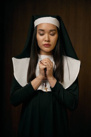 Foto de Retrato de religiosa rezando con los ojos cerrados sosteniendo rosario crucifijo. Joven hermosa virgen santa - Imagen libre de derechos