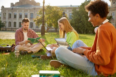Klassenkameraden sitzen zusammen auf grünem Gras im Campus-Park. Studentenfreundschaft, Jugend und Bildungskonzept