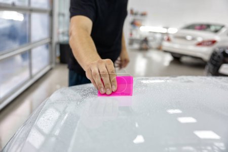 Photo for Crop view of professional skilled male master in car service applying armor film to hood. Auto detailing and maintenance garage workshop - Royalty Free Image