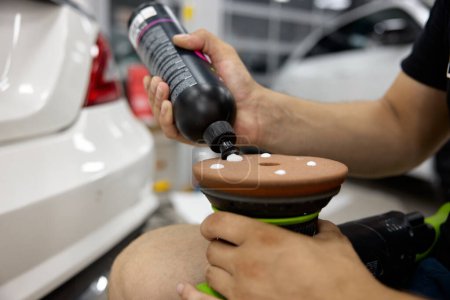 Man car service worker applying wax cream on disk of polisher machine. Transport maintenance workshop, carwash garage. Closeup view