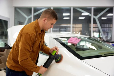 Photo for Man polishing his luxury sport car with applicator pad grinder in garage workshop - Royalty Free Image