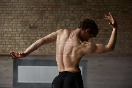 Téléchargez les photos : Ballet athlétique gracieux danseur masculin démontrant un haut du corps parfait fort. Shirtless musclé homme danse performer vue de dos - en image libre de droit
