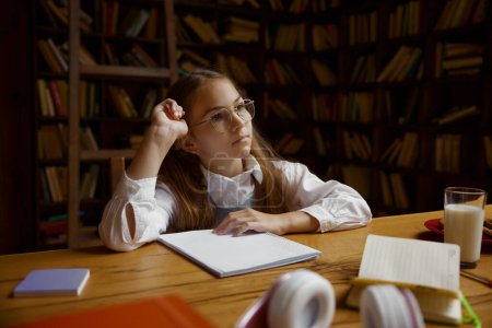 Photo for Portrait of pensive girl student doing homework or studying at desk in home library. Homeschooling concept - Royalty Free Image
