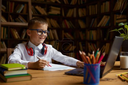 Photo for Overwhelmed little schoolboy in headset looking at laptop screen feeling misunderstanding and incomprehension. Difficulties and troubles at virtual lesson concept - Royalty Free Image